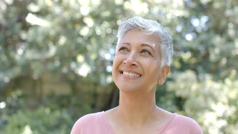 Retrato-De-Una-Feliz-Mujer-Birracial-Mayor-Con-El-Pelo-Corto-En-Un-Jardín-Soleado-En-Casa,-Cámara-Lenta