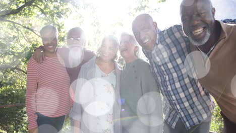 Animation-of-spots-of-light-over-diverse-senior-people-smiling-in-garden