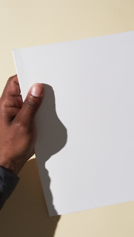 Vertical-video-of-hand-of-african-american-man-with-book-with-white-blank-pages-on-white-background