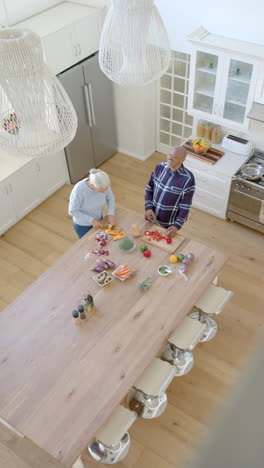 Vertical-video-of-happy-senior-biracial-couple-cooking-and-cutting-vegetables,-slow-motion