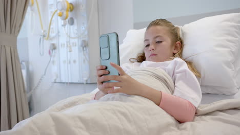 Caucasian-girl-patient-lying-in-hospital-bed-using-smartphone,-copy-space,-slow-motion