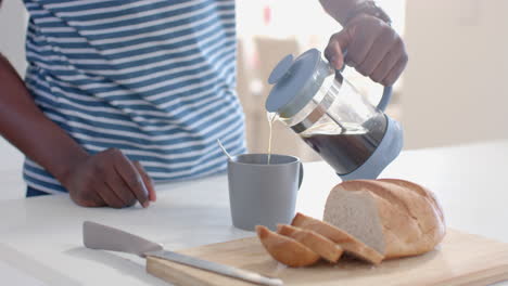 Hombre-Afroamericano-Vertiendo-Café-En-Una-Taza-En-Una-Cocina-Soleada,-Cámara-Lenta