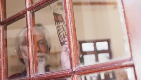 Happy-senior-biracial-business-owner-with-long-beard-changing-shop-sign-to-open,-slow-motion