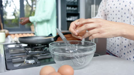 Biracial-couple-wearing-white-clothes-cooking-and-cracking-eggs-in-kitchen,-slow-motion