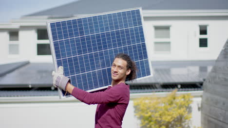 Retrato-De-Un-Hombre-Birracial-Feliz-Con-Guantes-Llevando-Panel-Solar-En-El-Jardín,-Cámara-Lenta