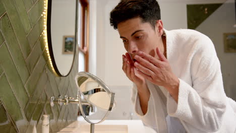 Focused-biracial-man-in-bathroom-inspecting-face-in-mirror,-slow-motion