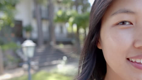 Half-face-of-happy-asian-woman-standing-and-smiling-in-sunny-garden,-slow-motion,-copy-space