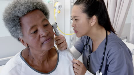 Doctora-Diversa-Que-Prueba-El-Oído-De-Una-Paciente-Mayor-En-La-Habitación-Del-Hospital,-Cámara-Lenta