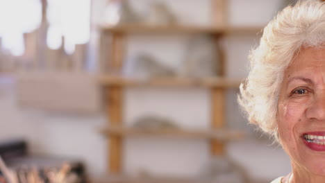 Half-face-of-biracial-woman-with-braided-hair-standing-and-smiling-in-pottery-studio,-slow-motion