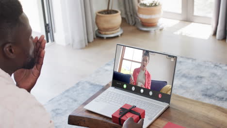 African-american-man-holding-gift-and-talking-with-caucasian-woman-on-laptop-screen