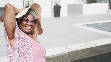 Happy-senior-african-american-woman-in-sunhat-sitting-on-terrace-in-sun,-copy-space,-slow-motion