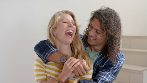 Portrait-of-happy-diverse-couple-embracing-sitting-on-stairs-at-home,-slow-motion