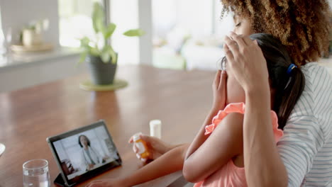 Biracial-mother-with-sick-daughter-at-home,-having-tablet-video-call-with-female-doctor,-slow-motion