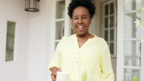 Feliz-Mujer-Mayor-Afroamericana-Caminando-Con-Una-Taza-Sonriendo-Fuera-De-Casa,-Cámara-Lenta