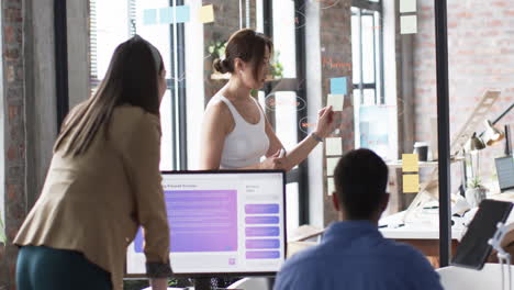 Young-Caucasian-businesswoman-presents-ideas-on-glass-wall-to-colleagues