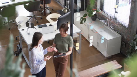 Young-Caucasian-woman-and-Asian-woman-discuss-business-over-a-tablet-in-an-office-setting