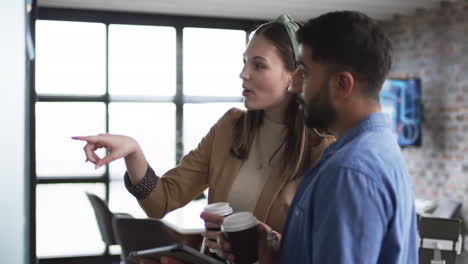 Young-Caucasian-woman-with-brown-hair-points-at-screen,-accompanied-by-a-young-Asian-man