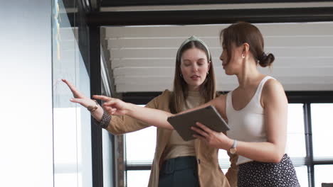 Young-Caucasian-woman-and-Asian-woman-discuss-business-over-digital-tablet-in-an-office-setting