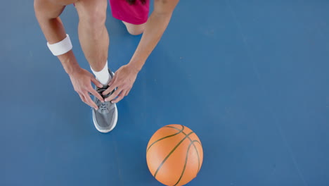 Un-Joven-Birracial-Se-Ata-Los-Cordones-De-Los-Zapatos-En-Una-Cancha-De-Baloncesto.