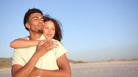 Una-Pareja-Birracial-Se-Abraza-En-Una-Playa-De-Arena-Durante-El-Día-Con-Espacio-Para-Copiar