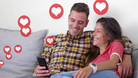 Animation-of-hearts-over-happy-diverse-couple-using-smartphone-at-home