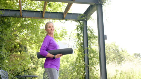 Una-Mujer-Caucásica-Mayor-Sostiene-Una-Estera-De-Yoga-Al-Aire-Libre,-Con-Espacio-Para-Copiar