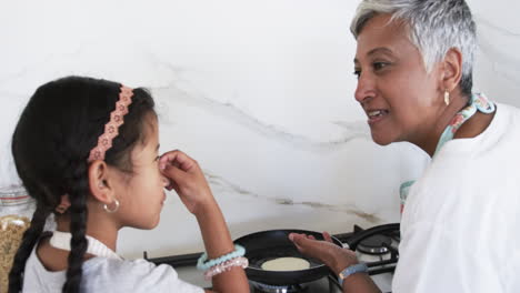 Biracial-granddaughter-with-a-headband-smiles-at-a-grandmother-with-short-gray-hair