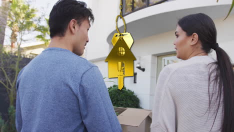 Animación-De-Una-Llave-Dorada-Y-Una-Casa-Sobre-Una-Pareja-Diversa-Llevando-Cajas-De-Cartón-En-Casa