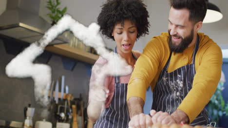 Animation-of-cloud-house-icon-over-happy-diverse-couple-cooking-in-kitchen