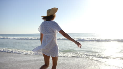 Una-Joven-Birracial-Disfruta-De-Un-Paseo-Por-La-Costa,-Su-Vestido-Blanco-Ondeando-Con-La-Brisa