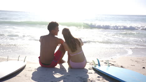 Biracial-man-and-Caucasian-woman-sit-close-on-a-sunny-beach