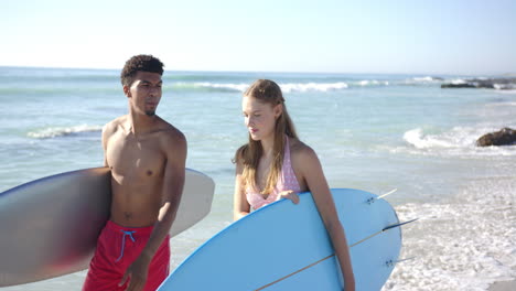 Biracial-man-and-Caucasian-woman-hold-surfboards-on-a-sunny-beach