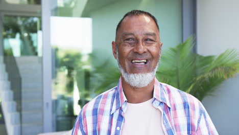 Biracial-man-with-a-warm-smile-stands-in-front-of-a-modern-home