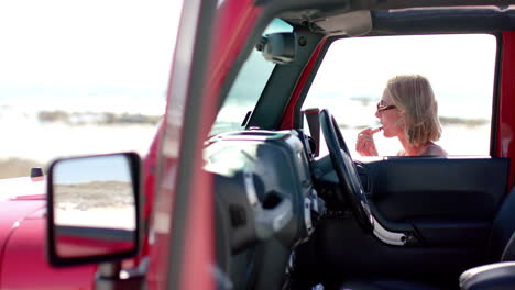 Young-Caucasian-woman-enjoys-a-drink-in-her-car-by-the-beach-on-a-road-trip