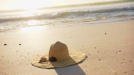 Un-Sombrero-De-Paja-Y-Gafas-De-Sol-Descansan-En-Una-Playa-De-Arena,-Bañada-Por-La-Luz-Del-Sol,-Con-Espacio-Para-Copiar