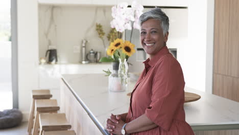 Biracial-woman-with-short-gray-hair-smiles-in-a-modern-kitchen-with-copy-space