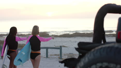 Una-Joven-Afroamericana-Y-Una-Joven-Caucásica-Practicando-Surf-Al-Amanecer,-Con-Espacio-Para-Copiar