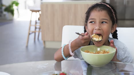 Biracial-girl-enjoys-a-bowl-of-cereal,-wearing-a-pink-headband-and-bracelets