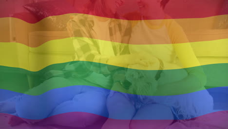 Animación-De-La-Bandera-Del-Arco-Iris-Del-Orgullo-Sobre-Una-Feliz-Pareja-De-Lesbianas-Caucásicas-Relajándose-En-El-Sofá-Con-Un-Perro-Mascota