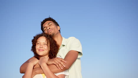 Biracial-Paar-Umarmt-Sich-Unter-Einem-Klaren-Blauen-Himmel,-Der-Mann-Hinter-Der-Frau-Mit-Seinen-Armen-Um-Sie