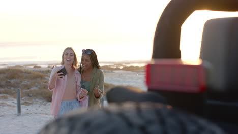 Young-African-American-woman-and-young-Caucasian-woman-pose-for-a-selfie-outdoors-on-a-road-trip,-wi