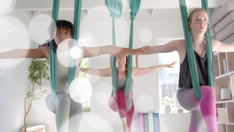 Animation-Von-Lichtpunkten-über-Zwei-Unterschiedlichen-Teenager-Mädchen,-Die-Aerial-Yoga-Machen-Und-Zu-Hause-Entspannen