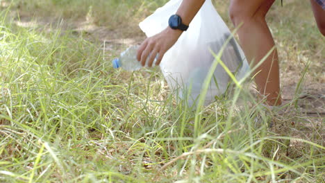 A-young-Caucasian-woman-is-picking-up-a-plastic-bottle-from-the-grass,-collecting-trash