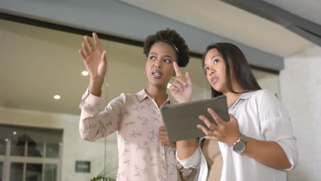 Asian-woman-and-African-American-woman-discuss-a-project-on-a-tablet-in-a-business-office-setting