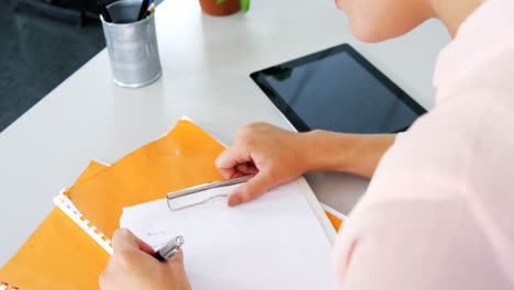 School-teacher-writing-notes-on-clipboard-in-classroom