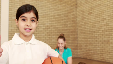 Niña-Sonriente-Con-Los-Pulgares-Hacia-Arriba-Sosteniendo-El-Baloncesto