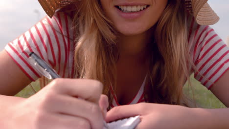 Mujer-Sonriente-Con-Sombrero-Escribiendo-En-El-Bloc-De-Notas