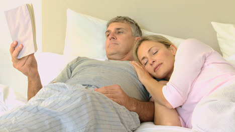 Attractive-man-reading-a-book-while-his-wife-sleeps-on-his-shoulder