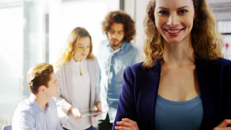 Woman-standing-with-arms-crossed-while-colleague-discussing-in-background