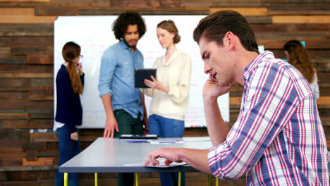 Business-executive-talking-on-mobile-phone-while-colleague-discussing-in-background